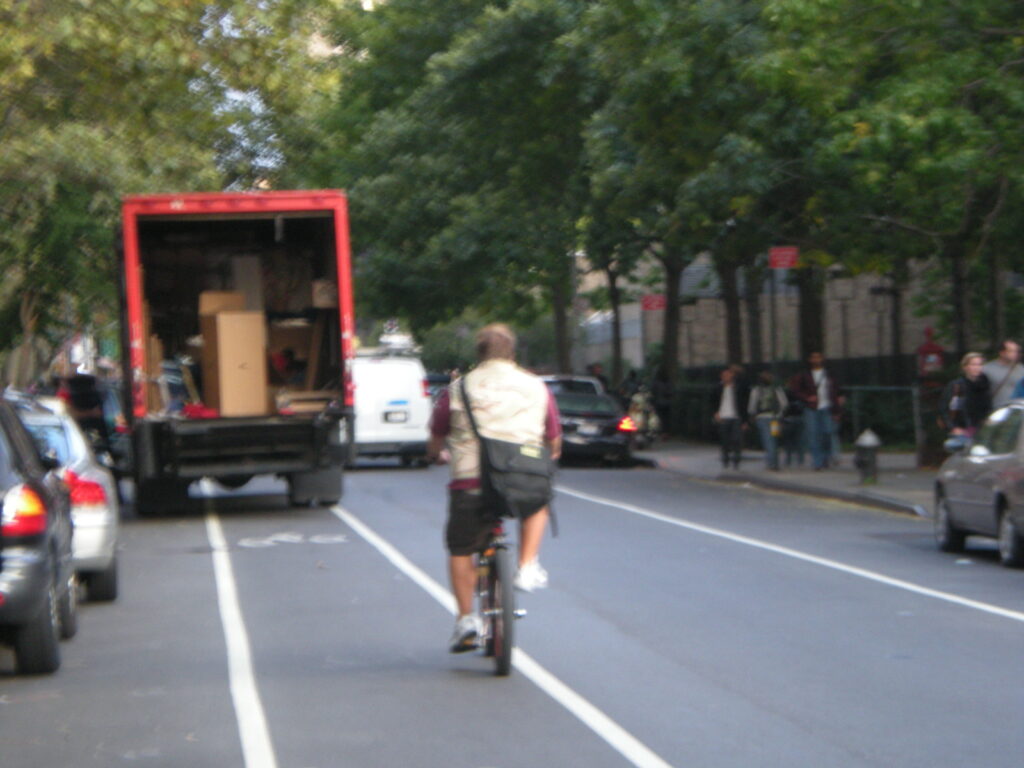 A moving van blocking a bike lane with a cyclist coming up behind the vehicle.